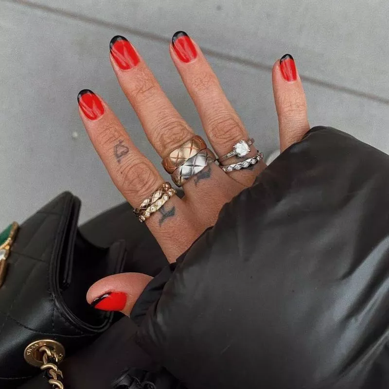 Red manicure with black tips and stacked mixed-metal rings