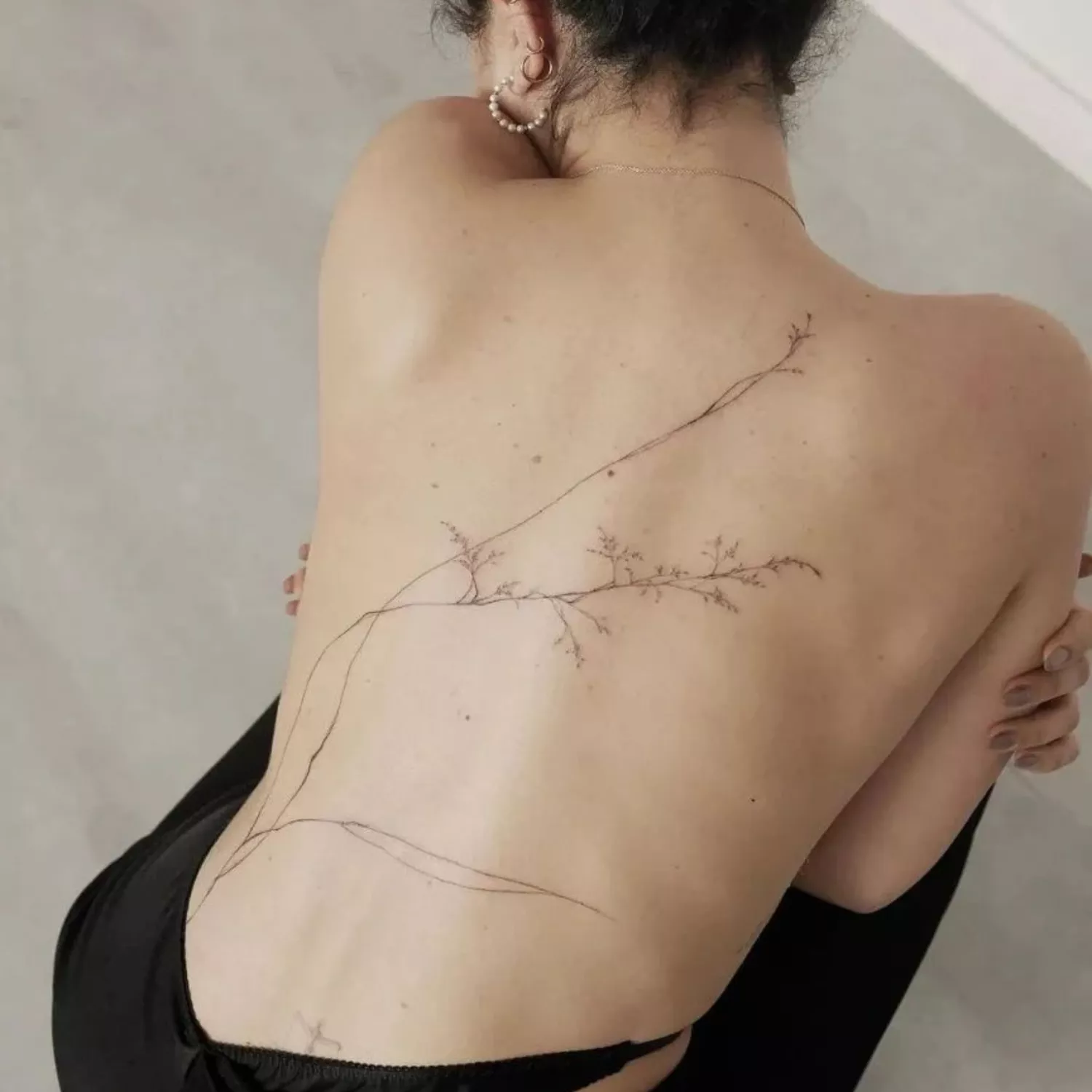 fine line back tattoo of branches and blossoms