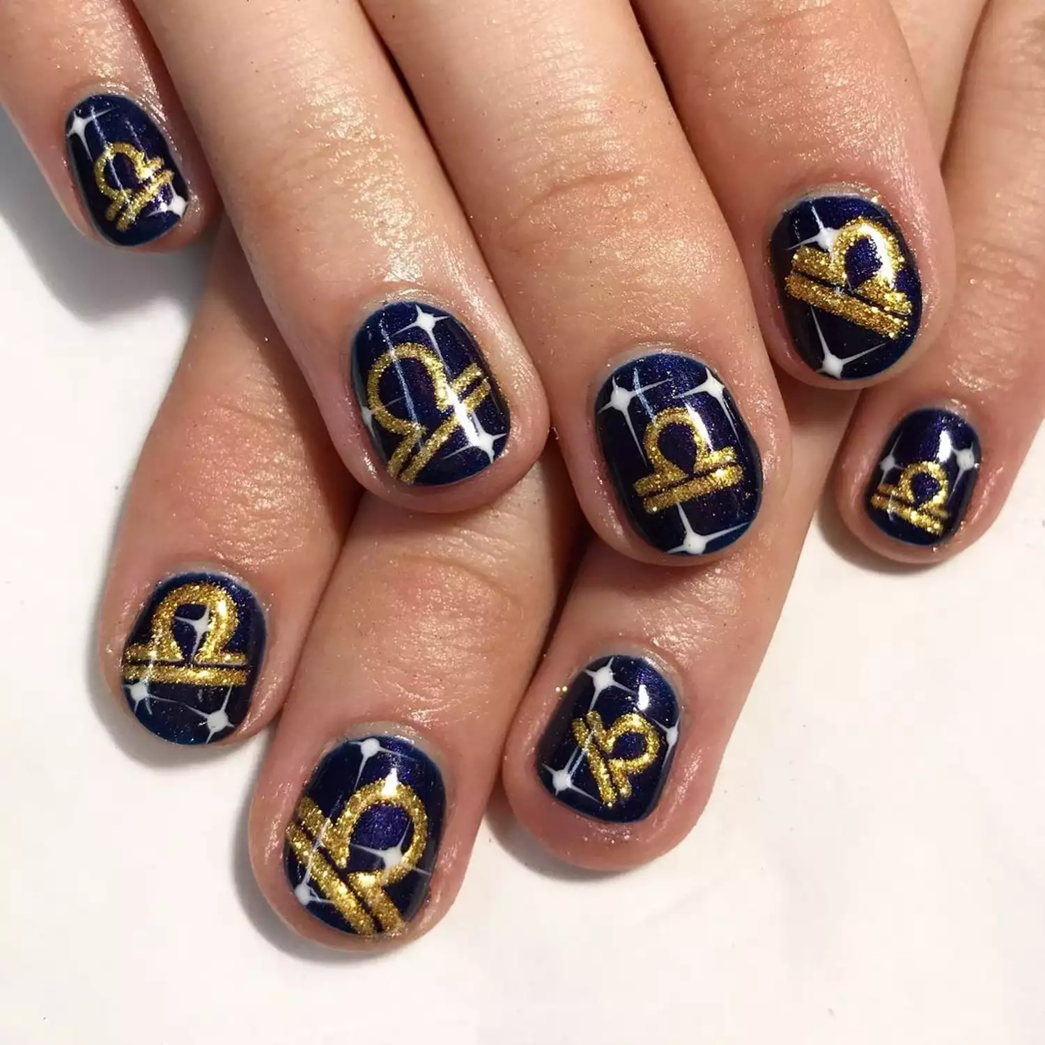 A blue manicure with Libra sign details in gold