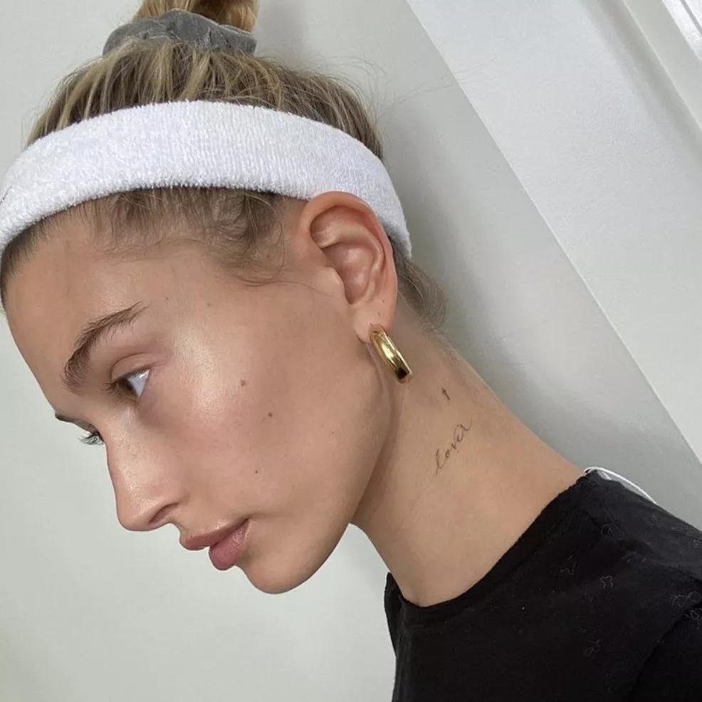 Hailey Bieber in a white sweatband showcasing her "lover" neck tattoo