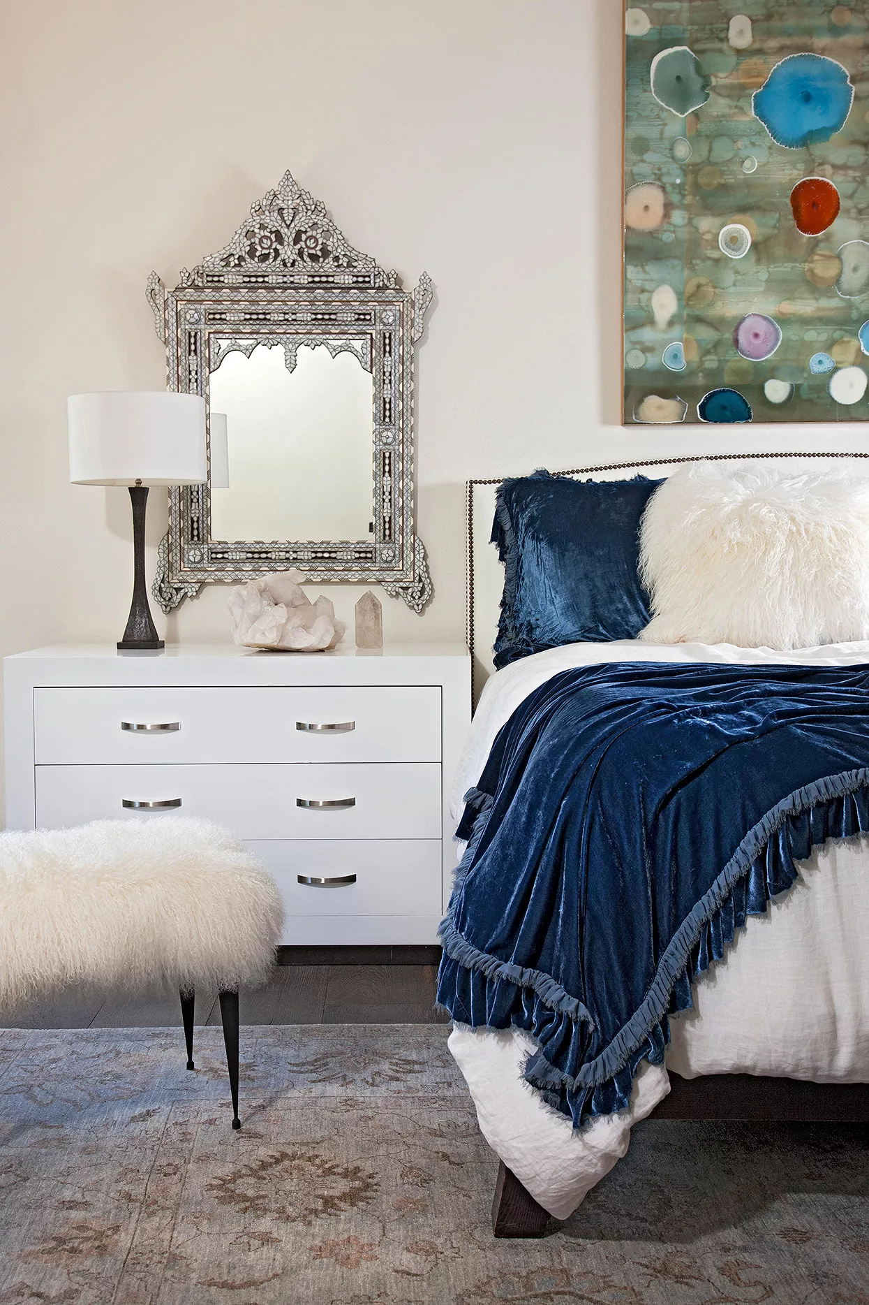 white bedroom with velvet throw, flokati stool and ornate silver frame