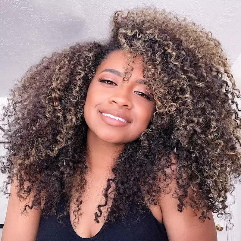 Woman with voluminous naturally curly hair with caramel highlights