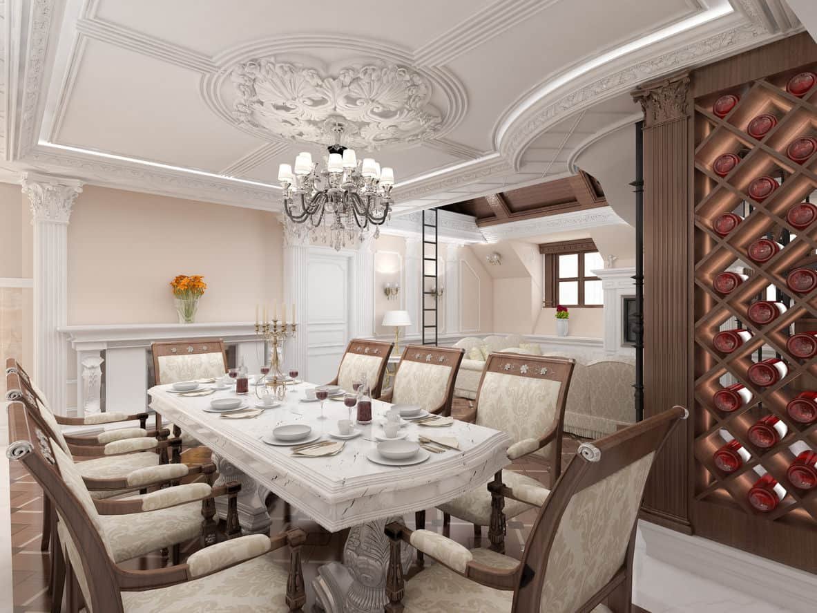 Luxury dining room with fleur patterned chairs and marble dining table lighted by a glamorous chandelier that hung from the tray ceiling designed with intricate details. It includes a fireplace and a built-in wine rack arranged in a crisscross pattern.