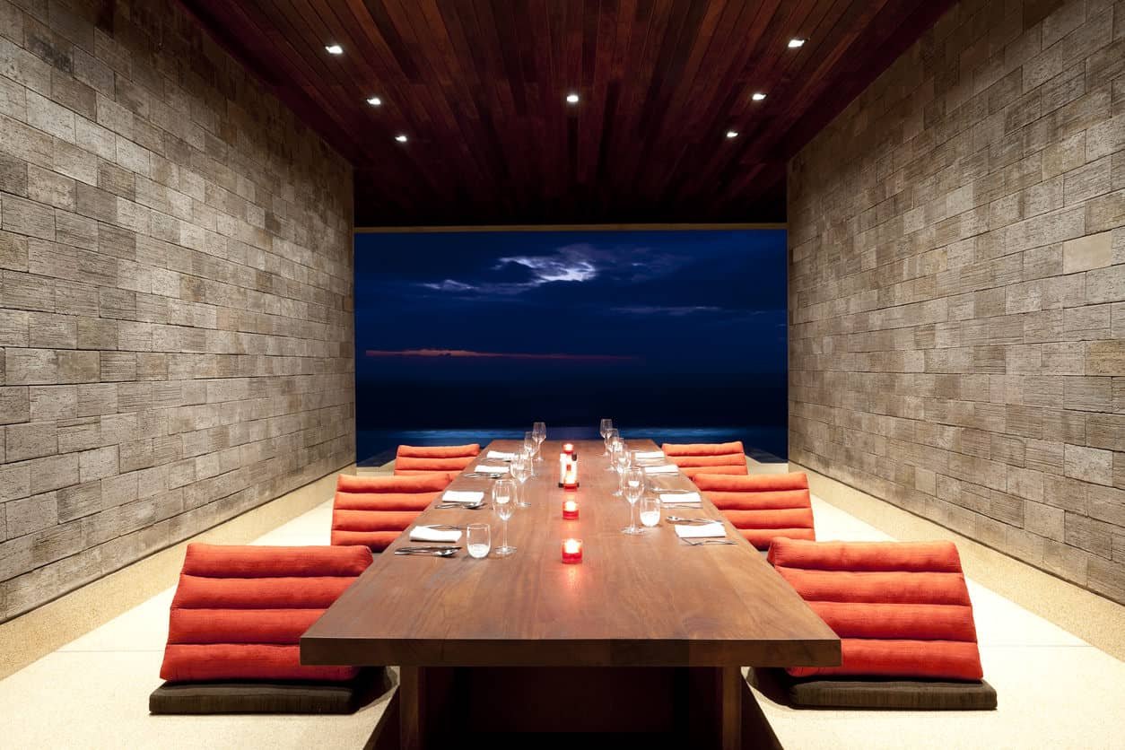 This one is a simple yet sleek dining room with brick walls and wood plank ceiling fitted with recessed lights. It has unique chairs and a long dining table facing a magnificent view.